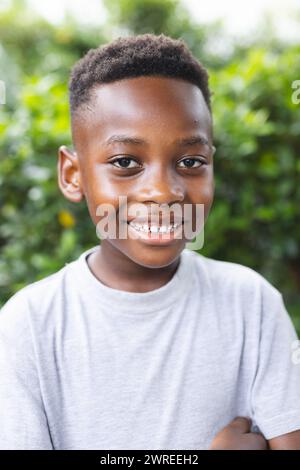 Garçon afro-américain avec un sourire lumineux se tient à l'extérieur dans un jardin Banque D'Images