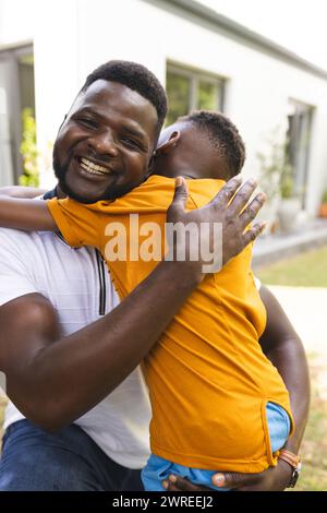Père afro-américain embrasse son fils, tous deux souriant joyeusement dans l'arrière-cour Banque D'Images