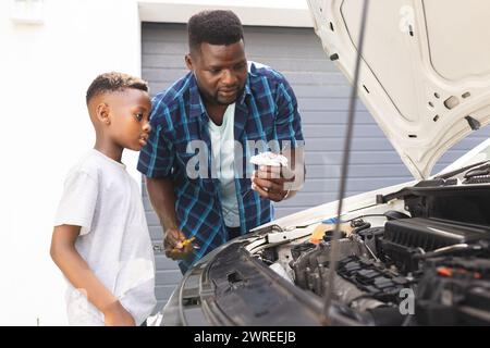 Père afro-américain enseigne à un fils l'entretien de la voiture Banque D'Images