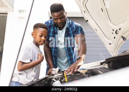 Père afro-américain enseigne à un fils l'entretien de la voiture Banque D'Images