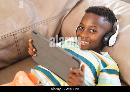 Garçon afro-américain avec un sourire éclatant portant des écouteurs et tenant une tablette Banque D'Images