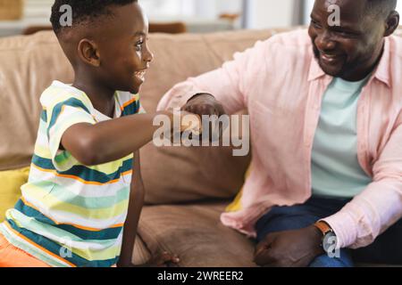 Père afro-américain et fils partagent une bosse de poing, souriant dans un cadre familial Banque D'Images