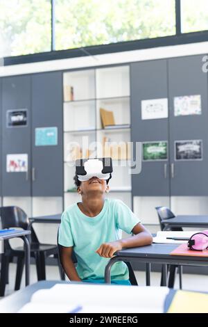 Garçon biracial portant un casque de réalité virtuelle dans une salle de classe à l'école Banque D'Images