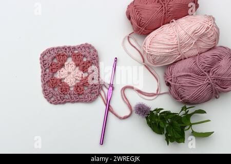 Carré Granny crocheté rose, boules de fil de coton doux de différentes nuances de couleur rose. Fond blanc avec espace de copie. Concept de crochet de ressort. Banque D'Images