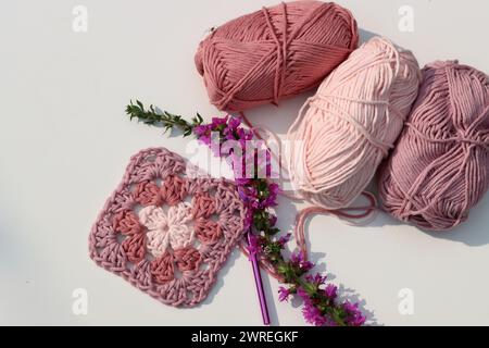 Carré Granny crocheté rose, boules de fil de coton doux de différentes nuances de couleur rose. Fond blanc avec espace de copie. Concept de crochet de ressort. Banque D'Images