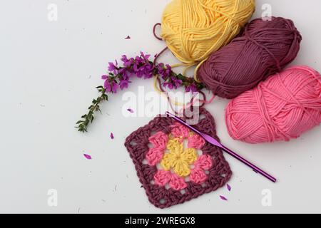 Carré Granny crocheté rose, boules de fil de coton doux de différentes nuances de couleur rose. Fond blanc avec espace de copie. Concept de crochet de ressort. Banque D'Images