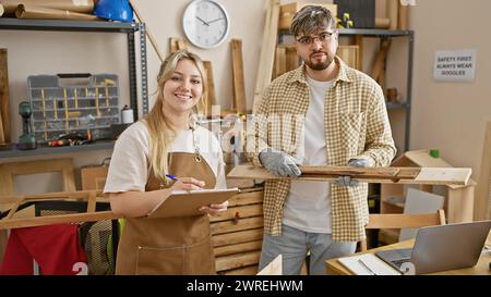 Une femme et un homme charpentiers dans un atelier, souriant alors qu’ils préparent des matériaux en bois, incarnant le partenariat et l’artisanat. Banque D'Images