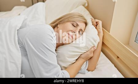 Une femme blonde paisible d'âge moyen dormant confortablement seule dans une chambre confortable. Banque D'Images