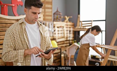 Homme et femme se sont concentrés sur leurs tâches dans un atelier de menuiserie lumineux, reflétant le travail d'équipe et l'artisanat dans un cadre intérieur. Banque D'Images