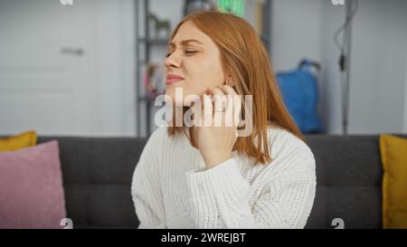 Une jeune femme caucasienne se gratte le visage dans le cadre intérieur confortable de sa maison. Banque D'Images