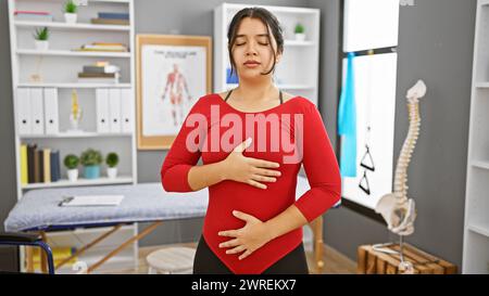 Une jeune femme hispanique pratique des techniques de respiration profonde dans la salle de rééducation d'une clinique, montrant un sentiment de calme et de concentration Banque D'Images