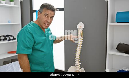 Médecin masculin confiant dans les gommages pointant vers un modèle de colonne vertébrale dans une clinique de rééducation lumineuse. Banque D'Images