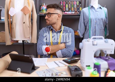 Homme hispanique avec barbe couturière designer travaillant à l'atelier regardant sur le côté avec les bras croisés convaincu et confiant Banque D'Images