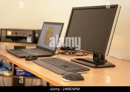 Intérieur de bureau à domicile avec table et deux ordinateurs dessus. Ordinateur de fond avec grand smiley dessus. Banque D'Images