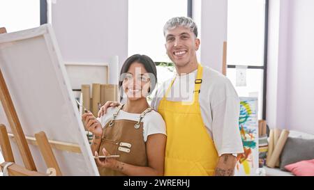 Une femme souriante et un couple d'hommes se tiennent ensemble dans un studio d'art, entouré de toiles et de matériel de peinture. Banque D'Images