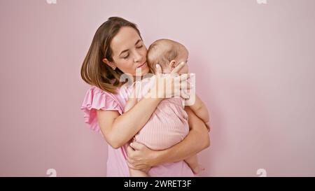Mère détendue serrant et tenant son bébé sur un fond frais et isolé rose, exprimant l'amour sérieux dans leur style de vie décontracté, strengthe Banque D'Images
