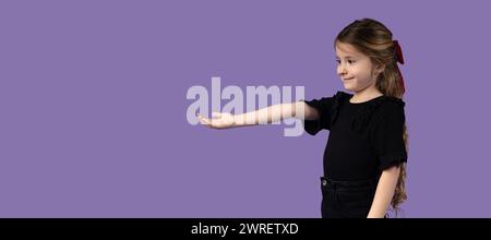 La petite fille blonde debout, la main tendue et regardant vers elle, sur un fond violet. La photo prise pour les bannières ou le produit p Banque D'Images