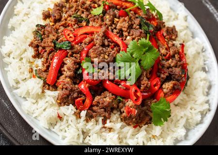 Sautez au basilic thaïlandais avec du bœuf, pad kra PAO, servi sur du riz au jasmin sur une assiette avec des baguettes sur une table en béton, gros plan Banque D'Images