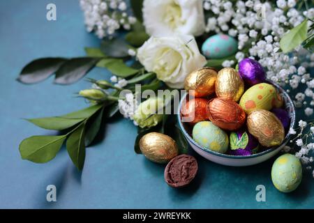 Oeufs de Pâques en chocolat enveloppés dans une feuille d'aluminium dans un bol en verre. Concept de célébration de Pâques. Nature morte colorée avec des bonbons. Fond texturé avec espace de copie. Banque D'Images