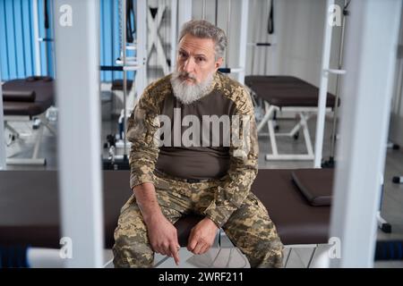 Homme militaire barbu assis dans le gymnase du centre de rééducation Banque D'Images