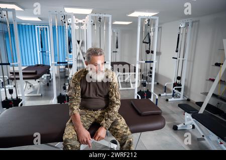 Militaire fatigué assis dans la salle de gym d'un centre de rééducation Banque D'Images