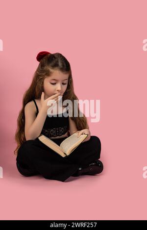 Peur girl holding open book contre fond rose, portrait, isolé sur fond rose, studio shot. kid a lire de l'information incroyable Banque D'Images