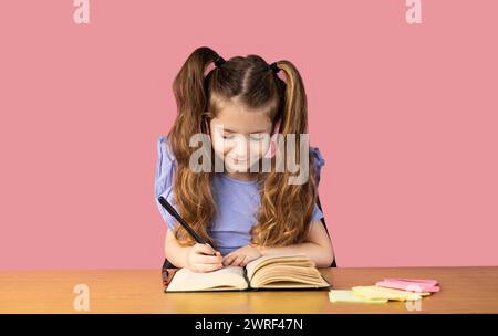 Une petite fille fait ses devoirs et est photographiée faisant des exercices, la petite fille est très excitée et fait ses devoirs avec grand plaisir. Élevé Banque D'Images