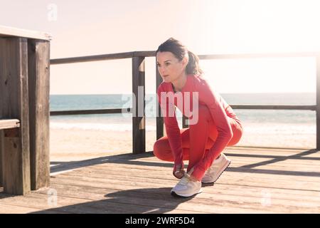 femme sportive jogger attachant ses lacets en préparation pour courir sur une promenade en bois au bord de la mer. Banque D'Images
