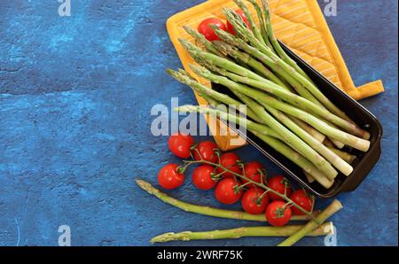 Asperges vertes fraîches et tomates cerises sur fond texturé bleu avec espace de copie. préparation saine du dîner. Concept d'alimentation équilibrée. Banque D'Images