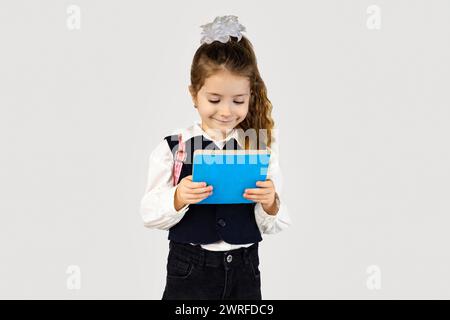 La petite fille tient joyeusement une tablette bleu électrique dans ses mains, avec un sourire sur son visage. Elle porte une tenue habillée avec un col et une manche Banque D'Images