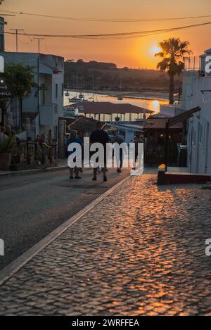 Vacanciers marchant sur Rua Dr Frederico Ramos Mendes vers le port d'Alvor, Portugal au coucher du soleil Banque D'Images