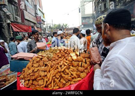 12 mars 2024, Dhaka, Wari, Bangladesh : les musulmans bangladais achètent de la nourriture pour rompre leur jeûne pendant le premier jour du mois de jeûne du Ramadan sur un marché alimentaire traditionnel au bazar de Chalk, à Dhaka, Bangladesh, le 12 mars 2024. Le mois sacré du Ramadan pour les musulmans est le neuvième mois du calendrier islamique, et on croit que la révélation du premier verset du Coran a eu lieu au cours de ses 10 dernières nuits. C’est aussi un moment de socialisation, principalement le soir après avoir rompu le jeûne, et un déplacement de toutes les activités vers la fin de la journée dans la plupart des pays. (Crédit image : © Habibur Rahman/ZUMA Pre Banque D'Images