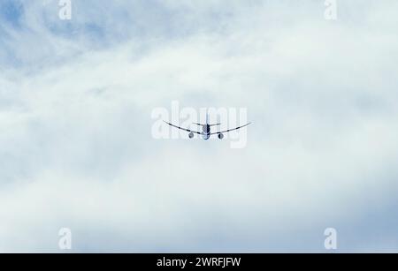 Un avion vole haut au-dessus du sol, coupant à travers d'épais nuages dans le ciel Banque D'Images