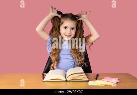 Folle petite fille regarde la caméra dans un studio isolé sur un fond rose tient ses mains sur son visage, souriant à la caméra. Phot de haute qualité Banque D'Images