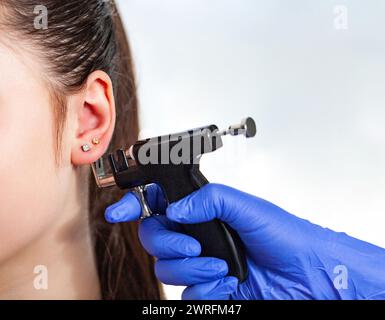 Femme ayant le processus de perçage d'oreille avec pistolet de perçage spécial dans le centre de beauté par travailleur médical, vue rapprochée. Photo de haute qualité Banque D'Images