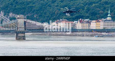Un hélicoptère militaire volant bas au-dessus d'un pont bondé près de l'architecture européenne classique et du Danube à Budapest Banque D'Images