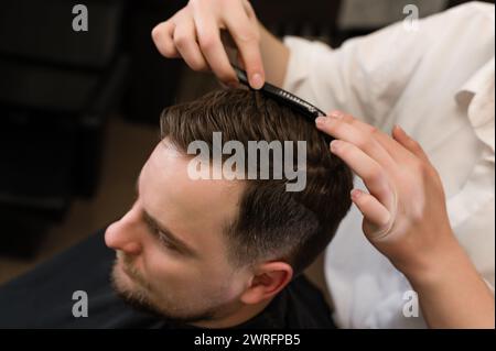 Coiffure avec un peigne, peignant les cheveux du client par un styliste. Coupe de cheveux d'un visiteur dans un salon de coiffure. Banque D'Images