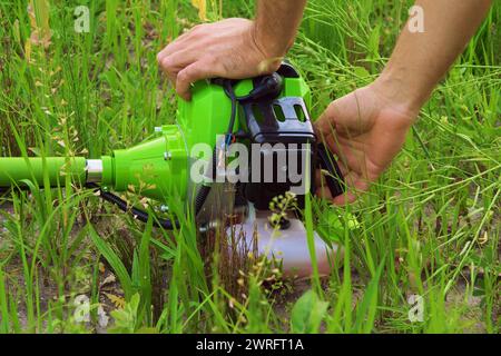 Main masculine démarrant une tondeuse à gazon sur fond d'herbe. Jardinier démarrer la tondeuse à gazon. La tondeuse à gazon professionnelle démarre son nouveau coupe-gazon à gaz. Ouvrier démarrer la tondeuse à gazon dans un pré avec de l'herbe. Banque D'Images