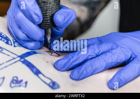 Photo horizontale vue rapprochée capturant la précision d'un tatoueur pendant qu'ils encrent un dessin, avec l'aiguille de la machine à tatouer dans une mise au point nette. Conce Banque D'Images