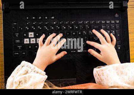 Une jeune fille utilise ses ongles pour taper sur le clavier d'un ordinateur portable, en utilisant le périphérique d'entrée pour appuyer sur les touches et la barre d'espace pour Banque D'Images