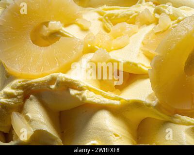 Glace glacée à l'arôme d'ananas - détail plein cadre. Gros plan d'une texture de surface jaune de crème glacée recouverte de morceaux de fruits. Banque D'Images