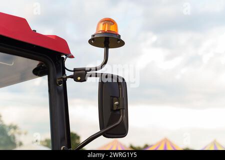 Gyrophare orange monté sur la cabine d'un tracteur agricole rouge, symbolisant la sécurité agricole, capturé sur fond d'un environnement partiellement nuageux Banque D'Images