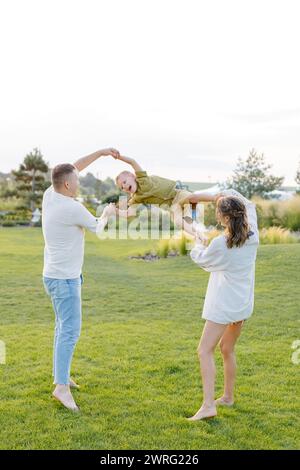 Une famille joue joyeusement dans l'herbe, s'adonnant à des activités amusantes avec son enfant. Les parents interagissent et tissent des liens avec leur petit o Banque D'Images