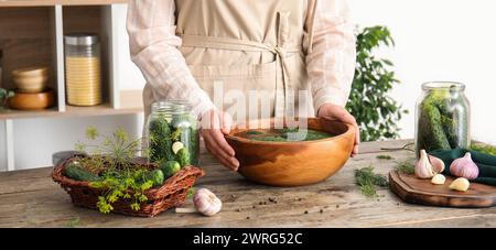 Femme préparant des concombres frais pour la mise en conserve à table dans la cuisine Banque D'Images