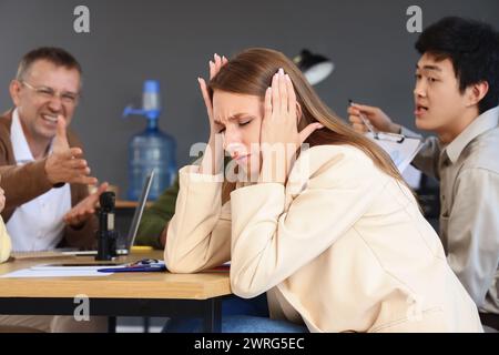 Jeune femme d'affaires souffrant de collègues bruyants dans le bureau Banque D'Images