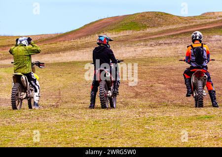 Trois individus aiment la moto dans un champ extérieur, manœuvrant leurs motos sur le terrain herbeux sous le ciel ouvert Banque D'Images