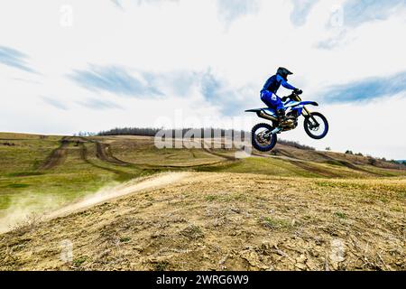 Une personne sur un vélo de motocross vole dans le ciel, son casque reflétant les nuages tandis que les roues du véhicule tournent en plein air Banque D'Images