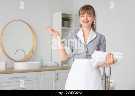 Jeune femme de chambre avec des serviettes propres dans la salle de bain Banque D'Images