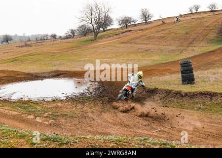 Une personne fait la course d'un moto de moto-cross sur une piste de terre, porte un casque et roule à travers l'herbe des hautes terres avec des pneus automobiles saisissant le terrai Banque D'Images