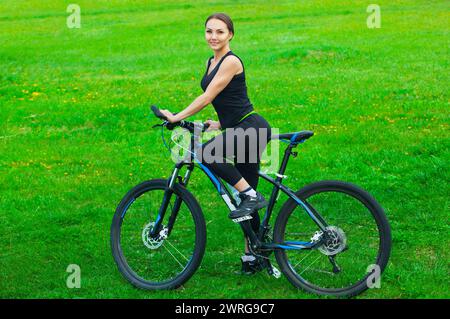 Jeune femme attrayante chevauchant un vélo de montagne dans un parc sur une pelouse verte au printemps. Banque D'Images